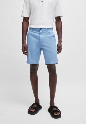 Pantalones cortos de color azul claro con una textura suave, con cierre de botón, bolsillos laterales y un corte recto. Combinados con sandalias negras.