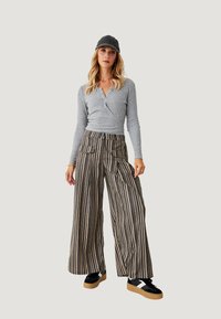 Top de manga larga de canalé gris con escote en V, combinado con pantalones de rayas anchas en beis y azul marino. Zapatillas negras con suelas beiges. Gorra gris.