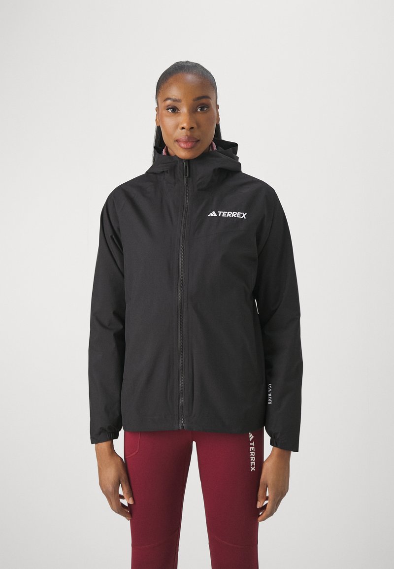 Black waterproof jacket with a hood, front zipper, and logo on left chest; paired with burgundy leggings featuring white accents.