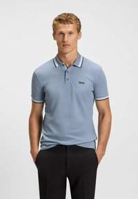 Hellblaues Polohemd aus strukturiertem Stoff, mit einem schwarz-weißen gestreiften Kragen undÄrmeln sowie einem kleinen schwarzen Logo auf der Brust.