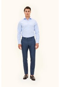 Hellblaues Hemd mit Knopfleiste, kombiniert mit dunkelblauen, maßgeschneiderten Hosen. Braune Lederloafer vervollständigen das Outfit. Keine Muster oder Strukturen sichtbar.