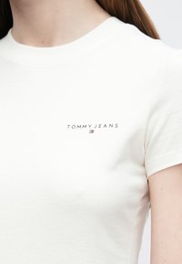 Bílé bavlněné tričko s přiléhavým střihem, krátkými rukávy a malým logem "TOMMY JEANS" na prsou v kontrastní barvě.