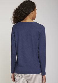 Langsleeve, navyblauwe top van zachte stof. Heeft een ronde halslijn en platte naden, gedragen met lichtgestreepte broek.