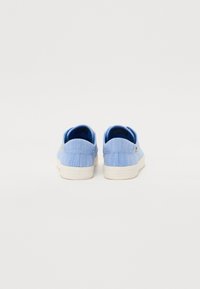 Scarpe slip-on in denim azzurro chiaro con superficie testurizzata, suola in gomma bianca e un piccolo logo sul lato. Rivetti sul tallone.