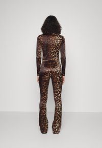 Overal s potiskem leopardího vzoru, který má přiléhavý střih, dlouhé rukávy a rozšířené nohavice. Vyrobený z lesklého materiálu, v bohatých hnědých a zlatých odstínech.