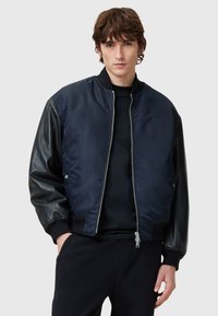 Navy bomber jacket with a shiny fabric body and matte black leather sleeves. Features ribbed cuffs and a front zip closure.