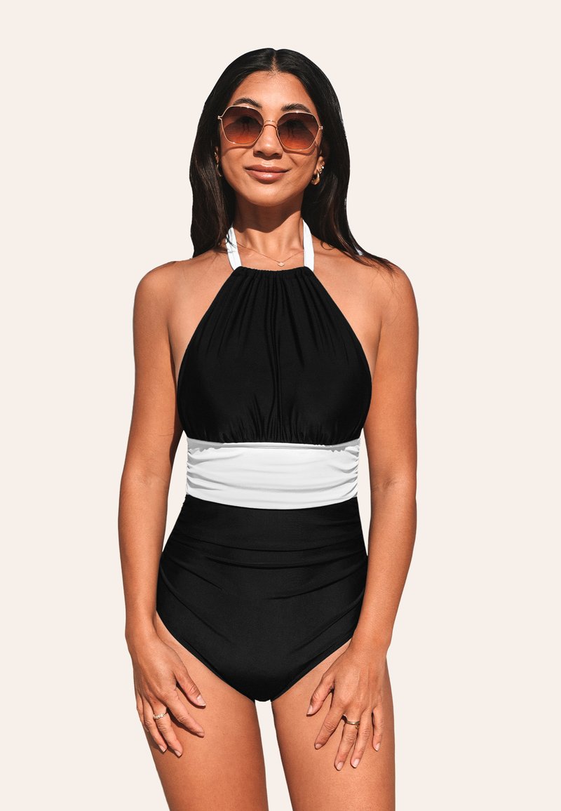 Bañador negro estilo halter con sección media blanca, que presenta tela recogida y parte inferior de talle alto. La modelo lleva gafas de sol redondas.