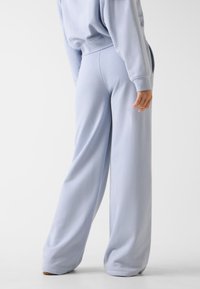 Jasnoniebieskie spodnie o szerokich nogawkach, wykonane z miękkiej tkaniny, z wysokim stanem i gładką teksturą, bez widocznych wzorów ani akcentów.