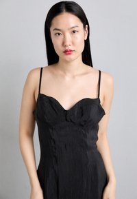 Robe noire sans manches avec un décolleté en cœur, réalisée en tissu léger et froissé, dotée de fines bretelles et d'une coupe ajustée.