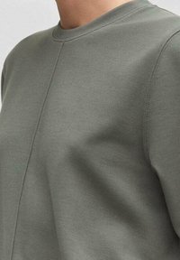 Kurzarmshirt mit Rundhalsausschnitt in Olivgrün, aus strukturierter Stoffqualität mit sichtbaren Nahtdetails, das eine lässige Passform bietet.