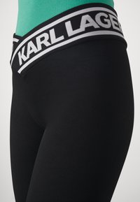 Zwarte leggings met een brede elastische tailleband met daarop de witte branding "KARL LAGERFELD", gemaakt van rekbare, gladde stof.