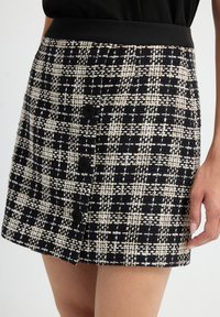 Falda de cuadros en blanco y negro, hecha de una tela texturizada, con una cinturilla ajustada y cuatro botones negros en la parte delantera.