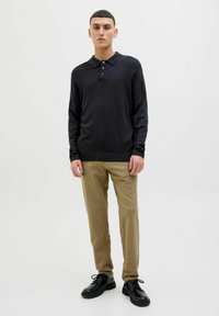 Svart langermet polo, lett strikket stoff, treknappslukking; parret med beige bukser og svarte snøresko. Minimalistisk design.