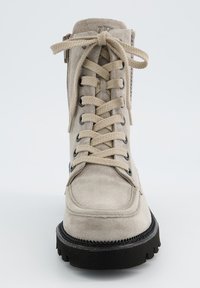 Botte en suède beige avec un bout rond, un laçage à l'avant et une semelle en caoutchouc noir. Présente une fermeture éclair sur le côté et un motif texturé autour de la tige.