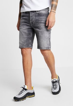 Szare spodenki jeansowe z denimu z wyblakłym wykończeniem, standardowym krojem, długością do kolan i pięciokieszeniowym designem, zestawione z czarno-żółtymi trampkami.