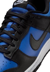 Detailní záběr černé a modré tenisky Nike s černými tkaničkami, černým logem Swoosh a bílou mezipodešví.