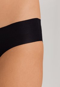 Mutande nere senza cuciture con una cintura ampia e comoda, texture liscia e taglio hipster, mostrate su uno sfondo di tono della pelle naturale.