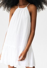 Vestido blanco de tirantes confeccionado en tejido ligero con acabado texturizado, con dobladillo en capas y tirantes ajustables para un ajuste holgado.