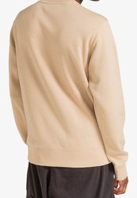 Sweat-shirt beige avec un col rond, des manches longues, et des poignets et une ceinture côtelés. Matière douce au toucher lisse, sans motifs visibles.