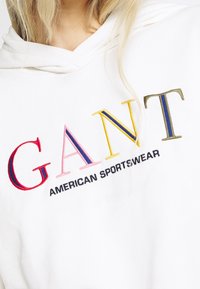 Sudadera blanca con el texto bordado en varios colores "GANT" en rosa, rojo, azul y amarillo, con "AMERICAN SPORTSWEAR" en negro debajo.