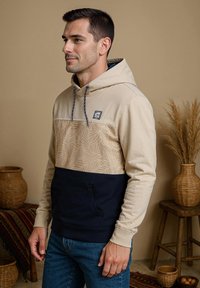 Beige en marineblauwe hoodie met een bladerenpatroon op het bovenste gedeelte, een kangoeroezak en een verstelbare trekkoordkap. Gemaakt van een katoenmengsel.