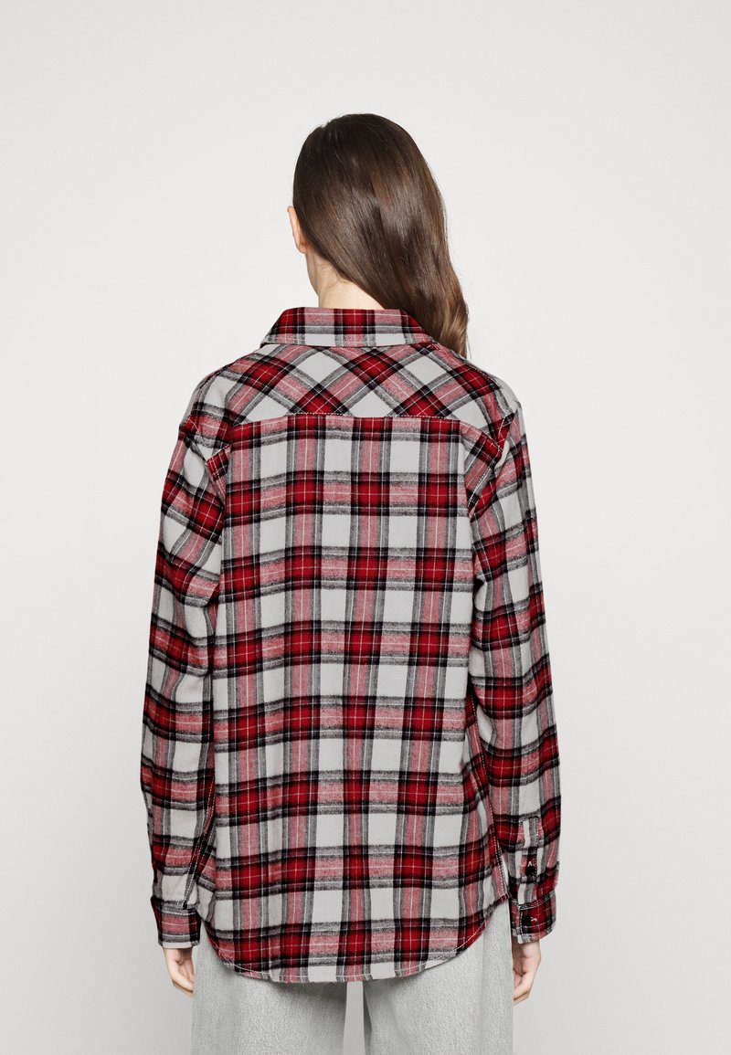 Koszula flanelowa w szarym kolorze z czerwono-czarnym wzorem w kraty. Posiada długie rękawy, kołnierz, mankiety zapinane na guziki oraz zaokrąglony dół z tyłu.