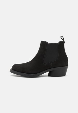 Schwarze Wildleder-Ankle Boots mit elastischen Seitenteilen und einer Zuglasche. Merkmale sind eine quadratische Zehenpartie und ein niedriger Blockabsatz. Glatte Textur und minimalistisches Design.