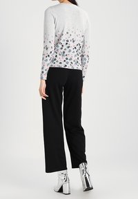 Ljusgrå tröja med blommönster, svarta vida byxor och metallics silverfärgade ankle boots, med en slät textur och figurnära design.