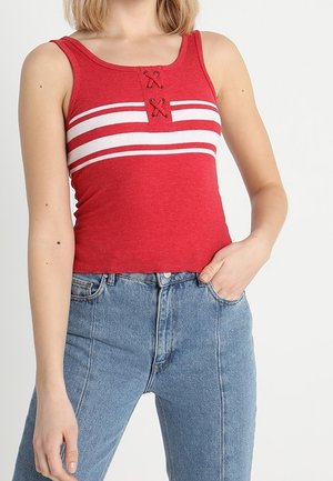 Rotes geripptes Tanktop mit weißen horizontalen Streifen und einem dekorativen Schnürdetail an der Brust, kombiniert mit hellblauen Denim-Jeans.