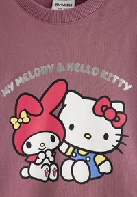 Lila sweatshirt med en grafisk bild av My Melody och Hello Kitty. Karaktärerna är utstansade i svart; My Melody bär en röd huva och ett gult band.