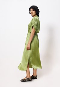 Satin grünes Kleid mit kurzen Ärmeln, elastischem Bund und seitlichen Schlitzen; kombiniert mit schwarzen Ballerinas im Leopardenmuster für den Kontrast.