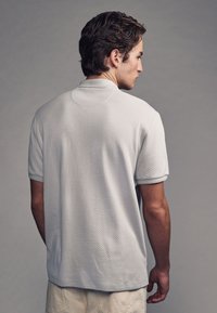 Helles graues Polohemd mit einem strukturierten Muster, kurzen Ärmeln und einem weichen Kragen. Einfaches, entspanntes Design, das sich für die Freizeitkleidung eignet.