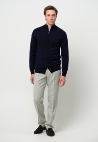 Sweater navy con cremallera y diseño ajustado, combinado con pantalones gris claro y mocasines de marrón oscuro. Material suave y acentos simples.