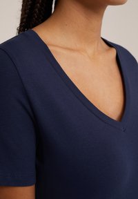 Navyblå v-ringad t-shirt gjord av mjuk bomullsblandning, med korta ärmar och en slät yta. Stygn detaljer vid ärmarna.