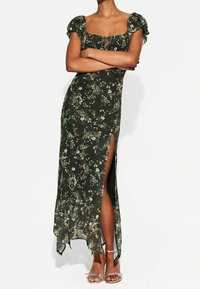 Floral-patterned, dark green maxi dress with puff sleeves, side slit, and ruffled hem. Lightweight fabric with a fitted bodice.