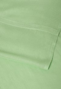 Tissu vert clair avec un tissage fin visible et des plis superposés soigneusement cousus.