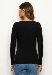 Langärmliges schwarzes Oberteil mit glatter Textur, rundem Ausschnitt, figurbetonter Silhouette und abgerundetem Saum, kombiniert mit blauen Jeans.