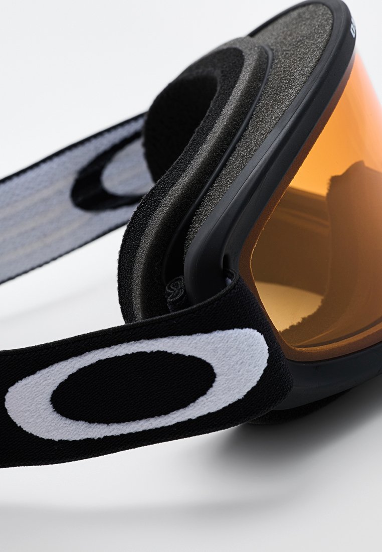 Zwarte skibril met een oranje lens, voorzien van een gestructureerd schuimframe en een stoffen band met een wit rond logo.