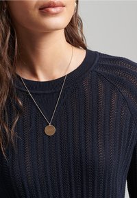 Granatowy sweter dzianinowy o ribbowanej teksturze i szerokim okrągłym dekolcie, z delikatną złotą naszyjnik z okrąłym zawieszką.