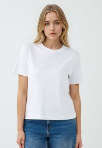 Witte katoenen T-shirt met korte mouwen, ronde halslijn, versierd met verspreide zilveren metallic versieringen op de voorkant.