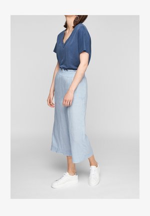 Blaues V-Ausschnitt-T-Shirt kombiniert mit hellblauen, weit geschnittenen Leinenhosen und weißen Turnschuhen. Die Hosen haben einen elastischen Bund und Saum.