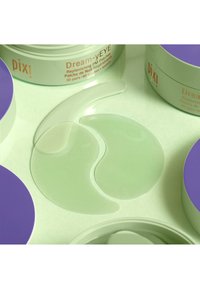 Gele Augenpflaster in einer hellgrünen, halbtransparenten Farbe mit glatter Textur. Umgeben von einer Verpackung mit einem lila Deckel und beschriftet mit "Dream-yEYE."