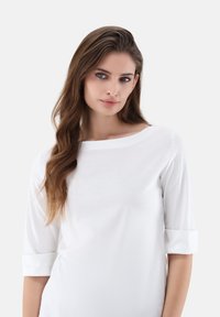 Weißes Oberteil mit drei Viertelärmeln, weitem Ausschnitt und umgeschlagenen Bündchen. Glatte Textur mit lockerer Passform, minimalistischem Design.