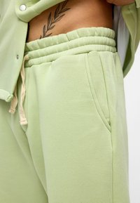 Lichtgroene sweatpants van zacht materiaal, met een elastische tailleband en trekkoord, en zijzakken.