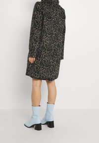 Manteau à imprimé léopard au design ajusté, présentant une palette de couleurs noire et marron. Associé à des bottines bleu clair et une jupe noire.