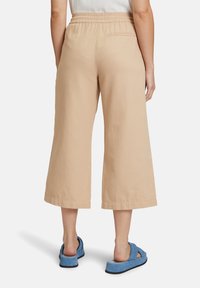 Beige cropped broek met een elastische tailleband en zijzakken, gecombineerd met blauwe instapsandalen. Glad, lichtgewicht materiaal.