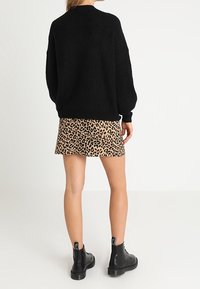 Schwarzer Strickpullover mit überschnittenen Schultern, kombiniert mit einem Minirock im Leopardenmuster. Schwarze Knöchelstiefel mit strukturierten Sohlen runden das Outfit ab.