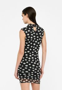 Schwarzes Kleid mit einer taillierten Silhouette, das mit weißen Punktmustern versehen ist. Ärmelloses Design mit einem Keyhole-Rückenausschnitt und transparenten Saumakzenten.