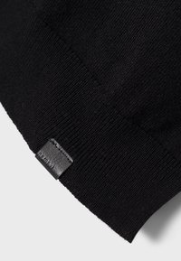 Maglione nero lavorato a maglia con texture a costine e orlo liscio. Presenta un piccolo etichetta in pelle sul bordo per un tocco di dettaglio.