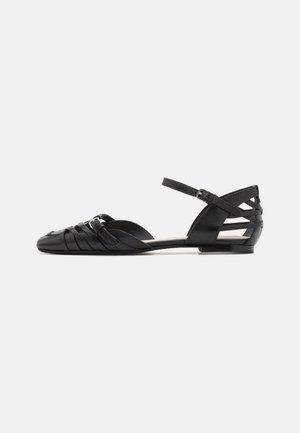 Schwarze flache Sandalen mit spitzem Zehenbereich, gekreuzten Riemen über dem Fuß, einem Knöchelriemen mit Schnalle und offenem Absatz mit mehreren horizontalen Riemen.